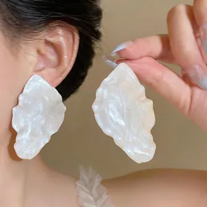 Detailed view of large white pearlescent leaf earrings with a metallic drip oil finish