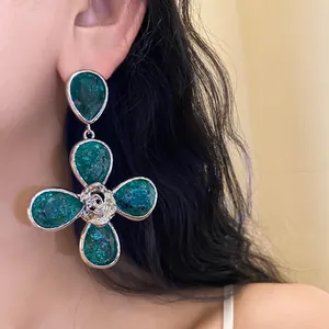 Close-up of oversized green resin flower earrings with metallic rose center on model.