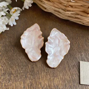 Close-up of elegant gold-bordered leaf earrings with pearlescent pink resin inlay.