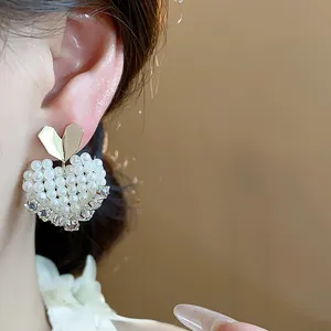Close-up of 14k gold plated heart pearl earrings worn on ear, French elegant style