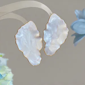 Close-up of elegant gold-trimmed leaf earrings with a pearlescent white finish