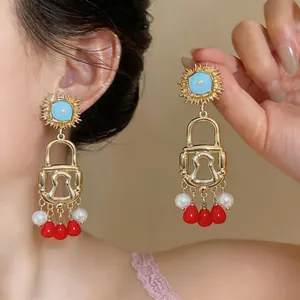 Dettaglio di orecchini vintage a forma di lucchetto con perle e gocce rosse pendenti.