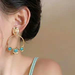 Large gold-toned hoop earrings with flower charms and turquoise stones worn by a model