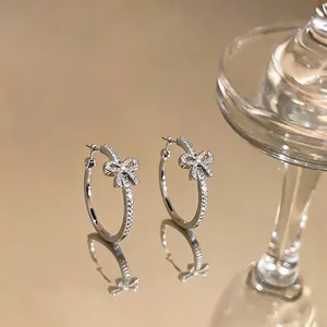 Elegant silver hoop earrings with sparkling bow design on a golden mirror background