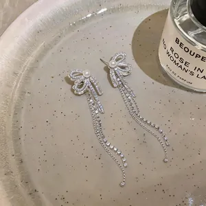Close-up of silver bow tassel earrings with sparkling zircons and pearl detail