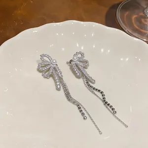 Macro detail of elegant silver bow earrings featuring zircon pave and long pearl tassels