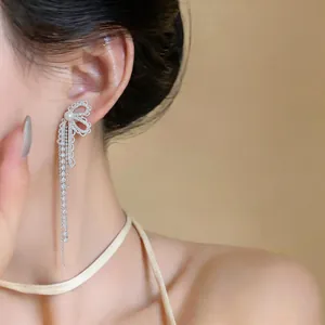Detailed view of silver bow-knot earrings featuring zircon tassels and a central pearl accent
