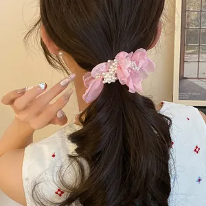 Detail view of a pink chiffon flower hair tie with delicate pearl accents on dark hair.