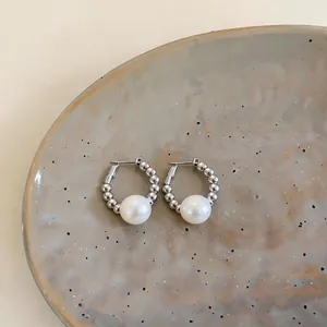 Close-up of elegant silver hoop earrings with a large pearl on a ceramic plate