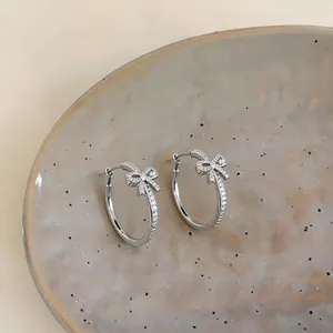 Detailed macro view of elegant silver bow-knot hoop earrings with pavé-set shimmering stones