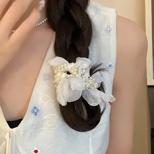 Close-up of a white chiffon floral scrunchie with pearl accents on a dark braided hair