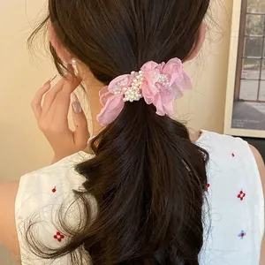 Close-up of a pink chiffon flower hair tie with pearl accents on a brunette ponytail