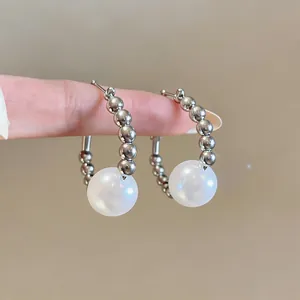 Macro detail of elegant silver hoop earrings featuring beads and a large white pearl