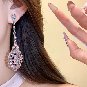 Dettaglio di orecchini pendenti vintage con strass rosa e blu indossati dal modello.