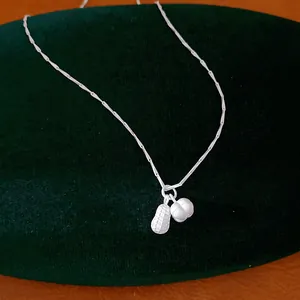 Macro view of minimalist silver peanut pendant necklace on a dark green velvet stand