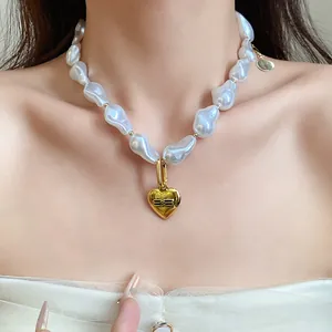 Close-up of baroque pearl necklace featuring a golden heart pendant with logo engraving