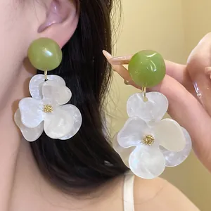 Macro detail of oversized white flower earrings with a green bead and pearly texture finish.