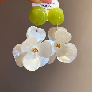 Detailed view of oversized white flower earrings with lime green studs and pearlescent petals