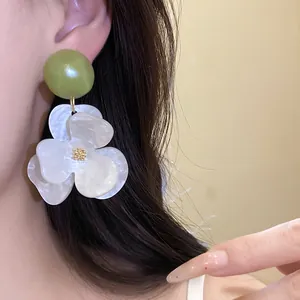 Close-up view of a large white flower earring with a green bead worn on an ear model