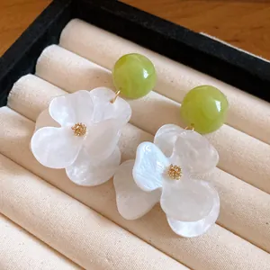 Close-up detail of elegant white flower earrings with green bead accents in a box