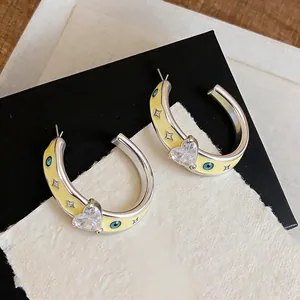 Detail of silver hoop earrings featuring yellow enamel, crystal heart and evil eye patterns
