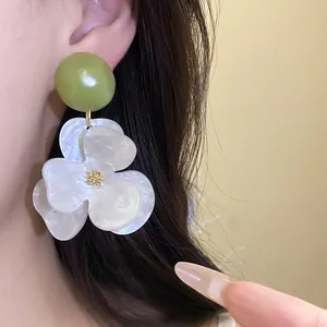 Detailed close-up of oversized white flower drop earrings with green bead on model