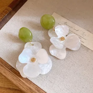 Macro view of elegant white resin flower earrings featuring green beads and gold accents.