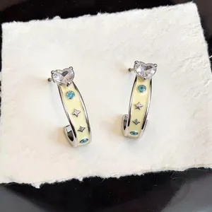 Close-up detail of silver heart stud earrings with yellow enamel and evil eye pattern