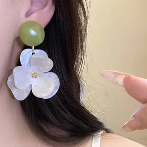 Close-up detail of oversized white flower earrings with iridescent petals and green bead