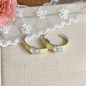 Detail view of yellow enamel hoop earrings with heart-shaped zircon and floral patterns