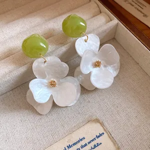 Close-up of elegant white pearlescent flower earrings featuring vibrant green resin beads
