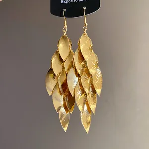 Dettaglio di orecchini a nappa con foglie dorate, texture in metallo spazzolato e stile retrò.