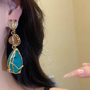 Detailed macro view of vintage gold-framed turquoise resin teardrop earrings on model