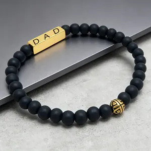 Close-up of masculine matte black agate bead bracelet with engraved gold DAD bar