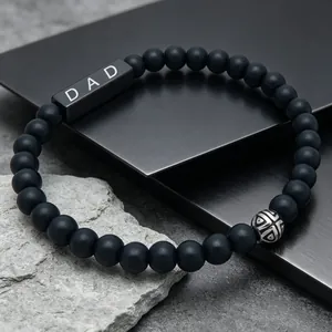 Macro view of engraved DAD block and patterned silver bead on black agate bracelet