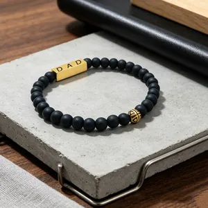 Detailed macro view of men's matte black beaded bracelet featuring a gold DAD bar