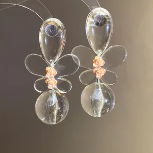 Detailed view of clear floral earrings with delicate pink flower accents and glass-like orbs