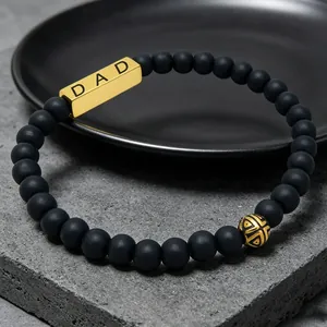Close-up of black matte natural stone bead bracelet with gold DAD engraved plate