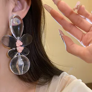 Detailed close-up showing oversized clear acrylic earrings featuring delicate pink floral charms