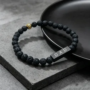 Detail of lava stone bracelet with DAD engraving and golden bead on stone background.