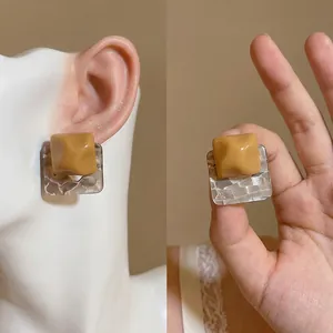 Unique resin square stud earrings with textured pattern shown on a model ear and hand