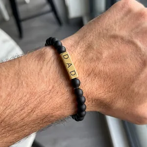 Close-up detail of a matte black agate bead bracelet with golden 'DAD' engraved square bead.