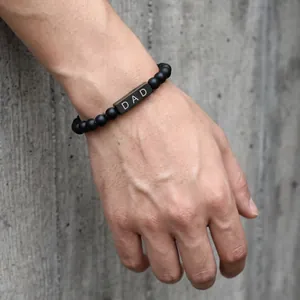 Close-up of men's matte black stone beaded bracelet with 'DAD' engraved metal bar