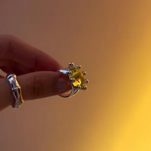 Detail of a silver-toned open ring with a round yellow resin stone and bead accents.