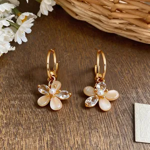 Close-up of dainty 18k gold plated flower earrings with zircon and shell petals.