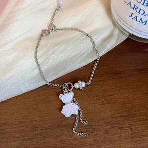 Nahaufnahme einer silbernen Halskette mit einem rosa Glasbär-Anhänger und einer Perle.
