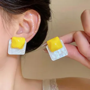 Detailed view of unique yellow and white pleated square resin stud earrings on ear.