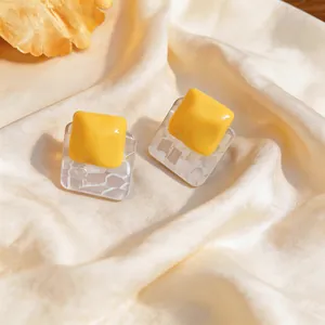 Detail shot of chic yellow resin square earrings on elegant pleated beige silk fabric