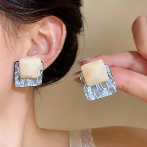 Macro detail of unique square resin stud earrings with pleated texture and silver pins