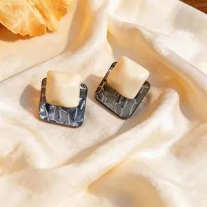 Close-up detail of geometric cream resin earrings with grey textured patterns